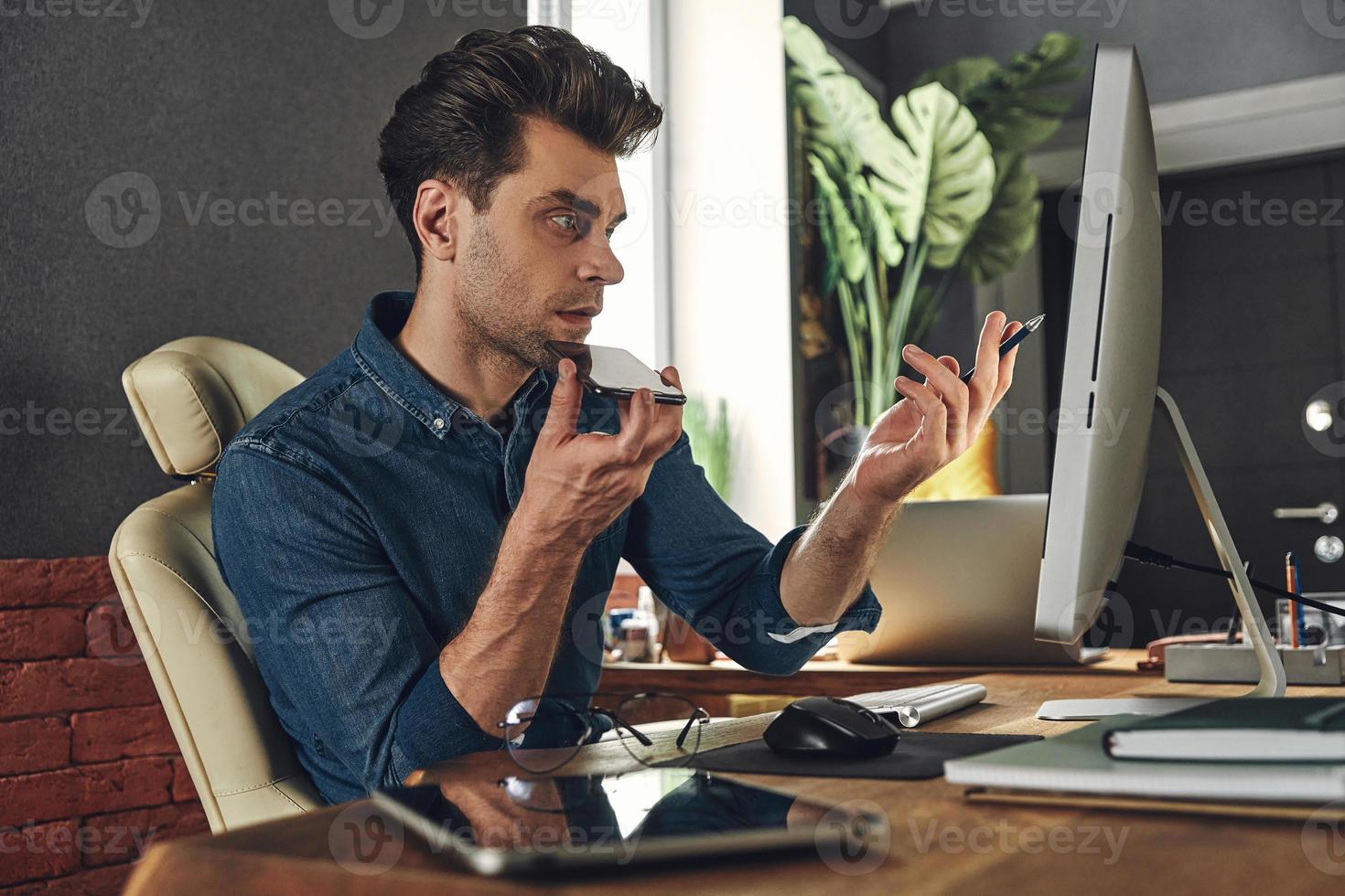 beau jeune homme utilisant un haut-parleur tout en parlant sur un téléphone portable au bureau photo