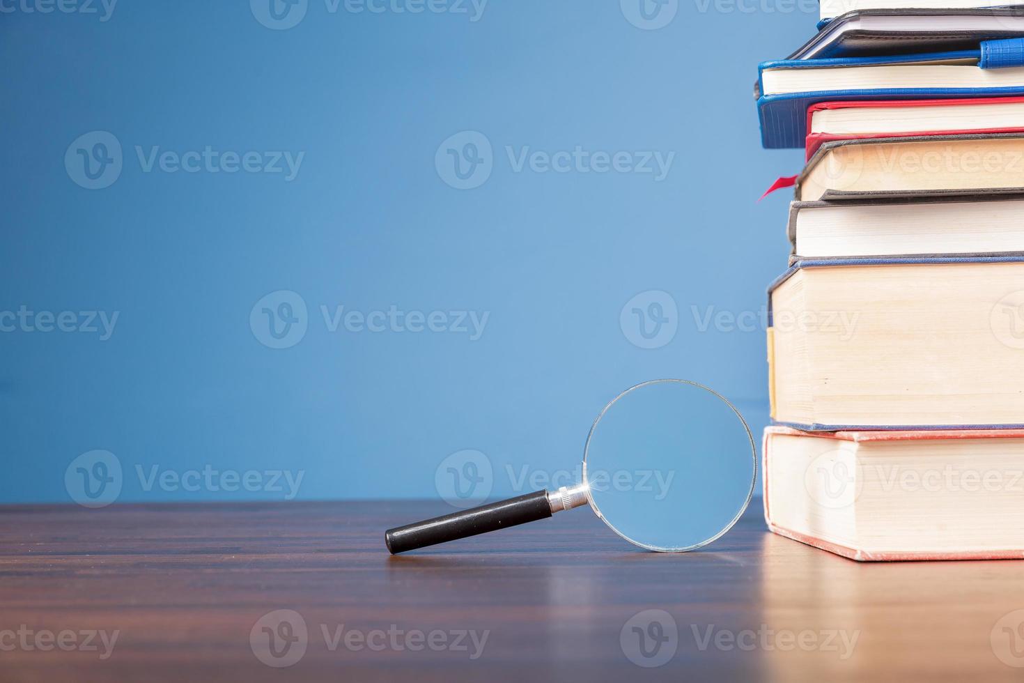 livre de pile avec loupe sur un bureau en bois dans la bibliothèque d'informations de l'école ou de l'université, concept pour l'éducation, la lecture, l'étude, l'espace de copie sur fond bleu. photo