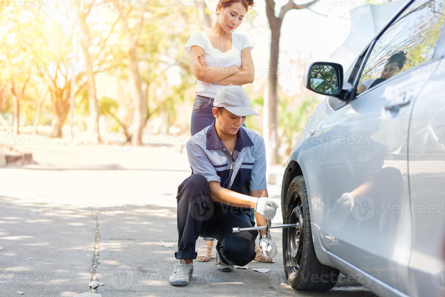 expertise mécanicien homme en uniforme utilisant la force essayant de dévisser les écrous de boulons de roue et aider une femme à changer de roue de voiture sur l'autoroute, service de voiture, réparation, concept d'entretien. photo