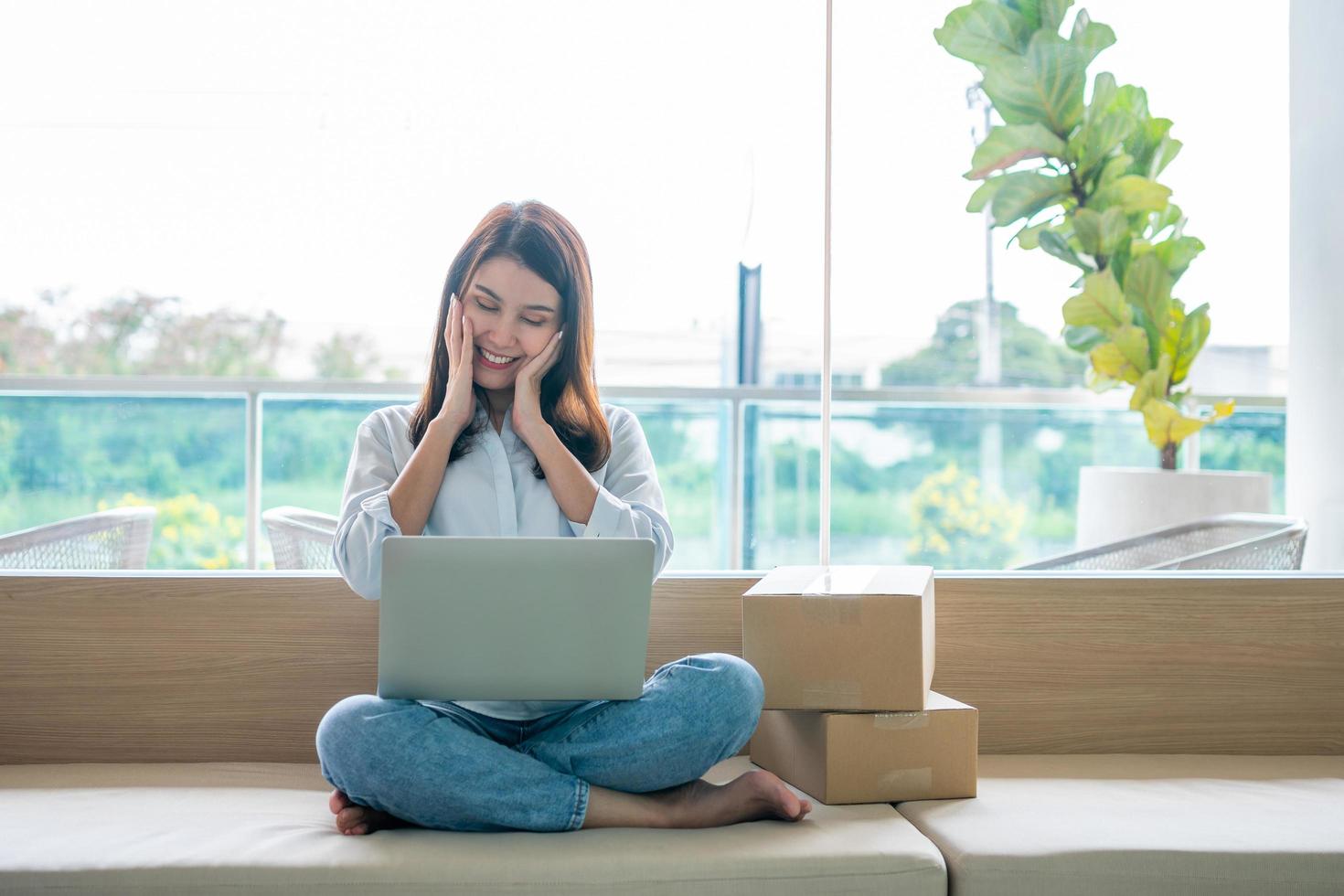 heureuse jeune femme entrepreneure asiatique, sourire pour le succès des ventes après avoir vérifié la commande du magasin d'achat en ligne dans un ordinateur portable au bureau à domicile, concept d'entreprise marchande en ligne et de commerce électronique photo