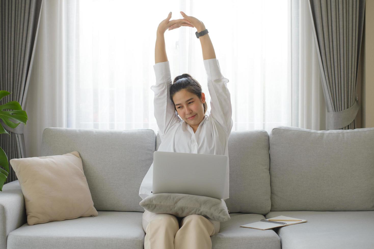 femme d'affaires portant une chemise blanche assise sur un canapé avec un ordinateur portable levant les bras au-dessus de sa tête s'étirant pour soulager la douleur après s'être assise longtemps au travail. photo