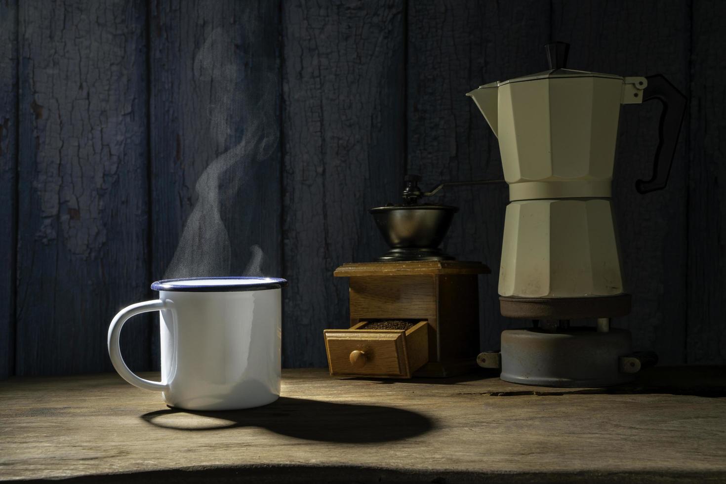 tasse de café émaillée avec de la fumée. ensemble de café avec pot de moka et broyeur sur le vieux plancher en bois. mise au point douce. photo