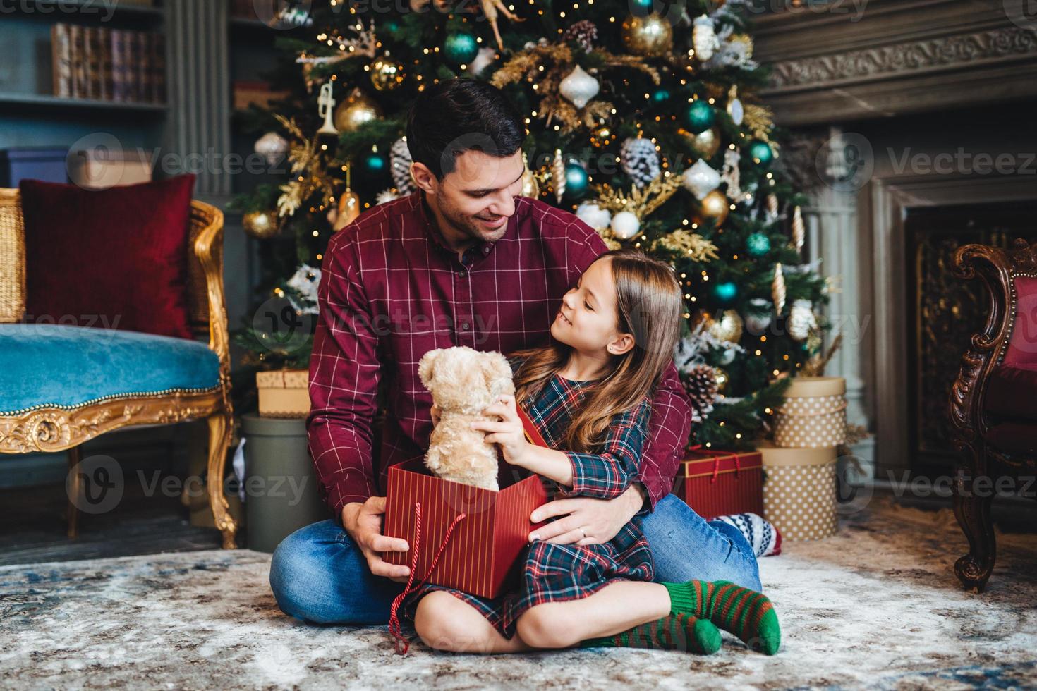 une petite fille tient un ours en peluche, reçoit un cadeau inattendu d'un père affectueux, lui étant reconnaissant. le jeune papa donne un cadeau à sa fille, la félicite pour noël ou le nouvel an photo
