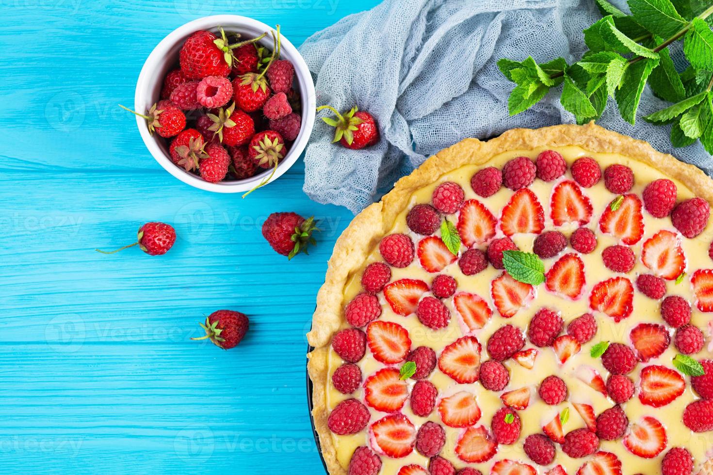 délicieuse tarte maison aux fraises et framboises garnie de feuilles de menthe sur fond de bois bleu. vue de dessus photo