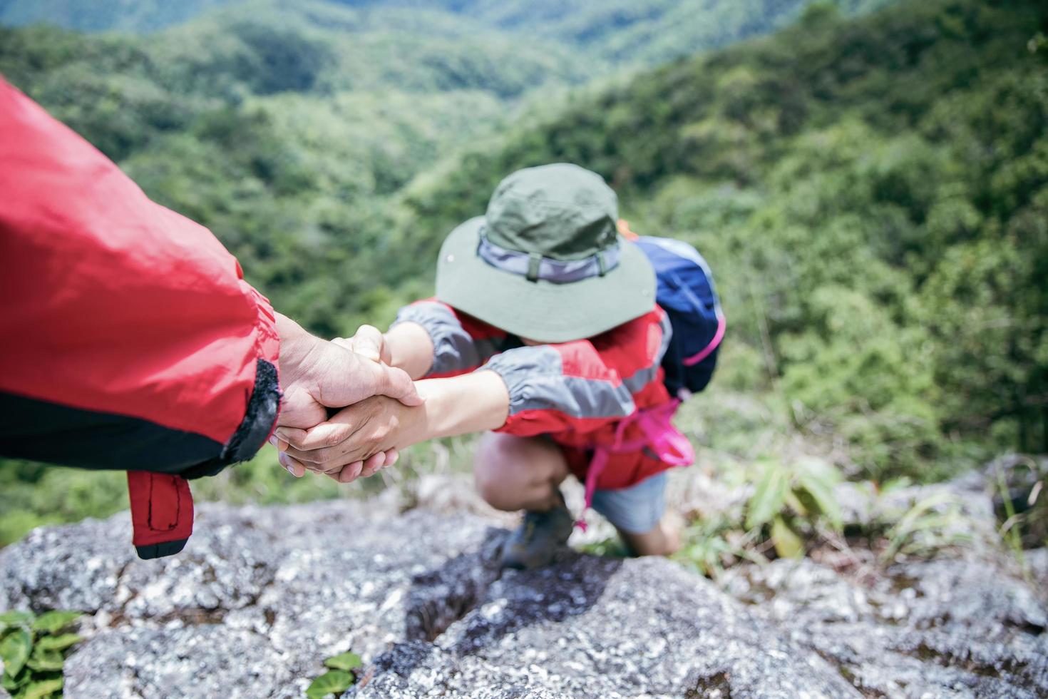 une personne fait de la randonnée avec des amis qui s'entraident sur une montagne. homme et femme donnant un coup de main et mode de vie actif. un couple d'asie en randonnée s'entraide. concept d'amitié, travail d'équipe. photo