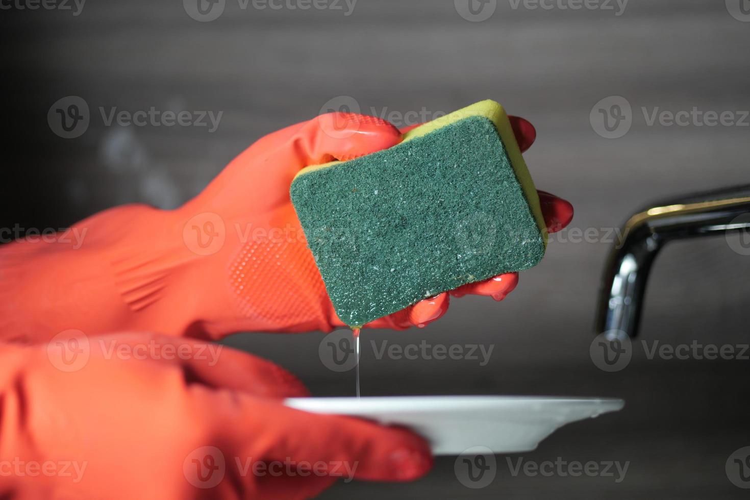 main dans la plaque de nettoyage des gants en caoutchouc de couleur rouge avec une éponge photo