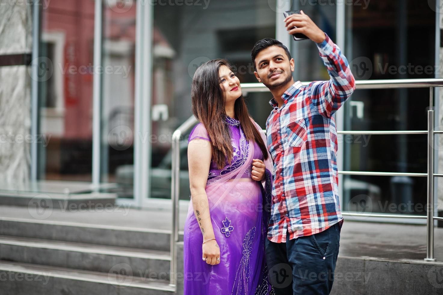 élégant couple hindou indien posé dans la rue et regardant un téléphone portable et faisant un selfie ensemble. photo