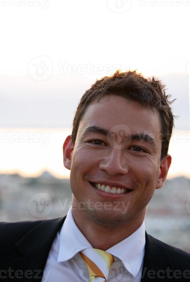 beau et souriant jeune homme vêtu d'un costume pendant le coucher du soleil photo