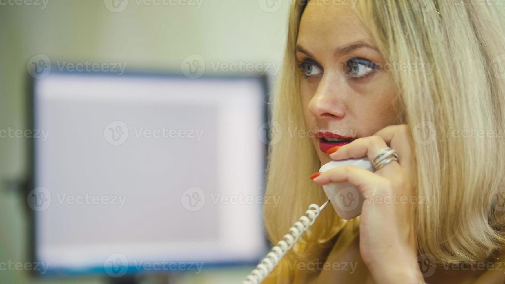 jeune femme blonde au bureau parlant au téléphone devant l'ordinateur, gros plan photo