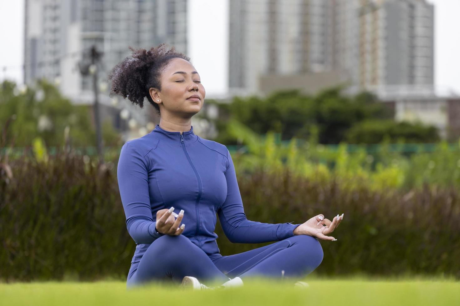 femme afro-américaine pratiquant de manière relaxante la méditation dans le parc public avec vue sur la ville urbaine pour atteindre le bonheur de la sagesse de la paix intérieure pour un esprit et une âme sains photo