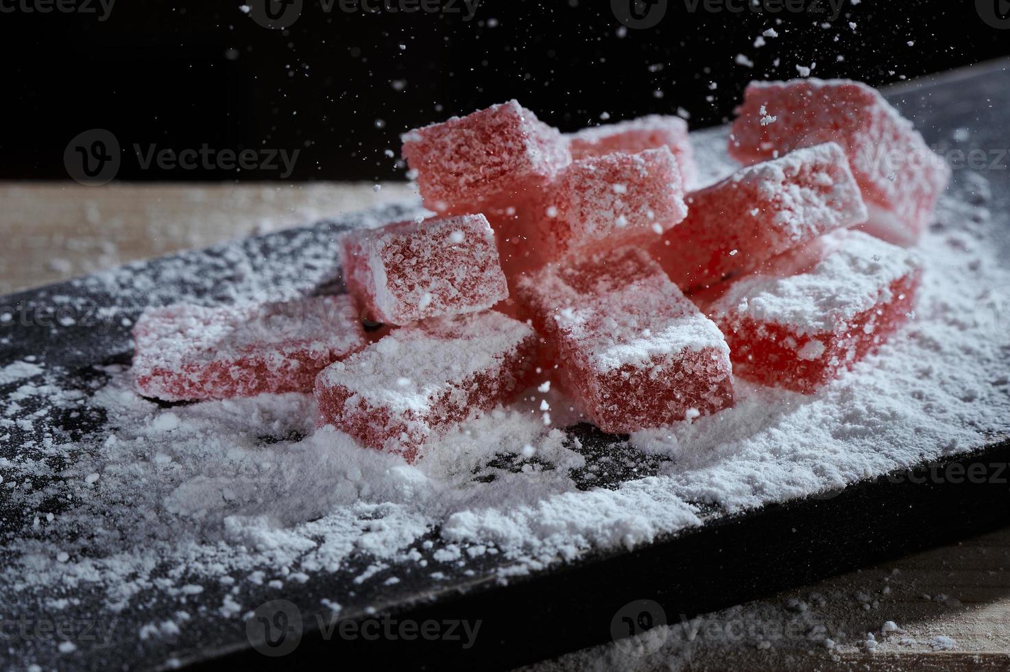 le sucre en poudre est saupoudré sur des bonbons à la gelée de marmelade de baies sur une planche à découper en bois sur fond noir. délice turc traditionnel lokum bonbons mous enrobés de sucre. photo