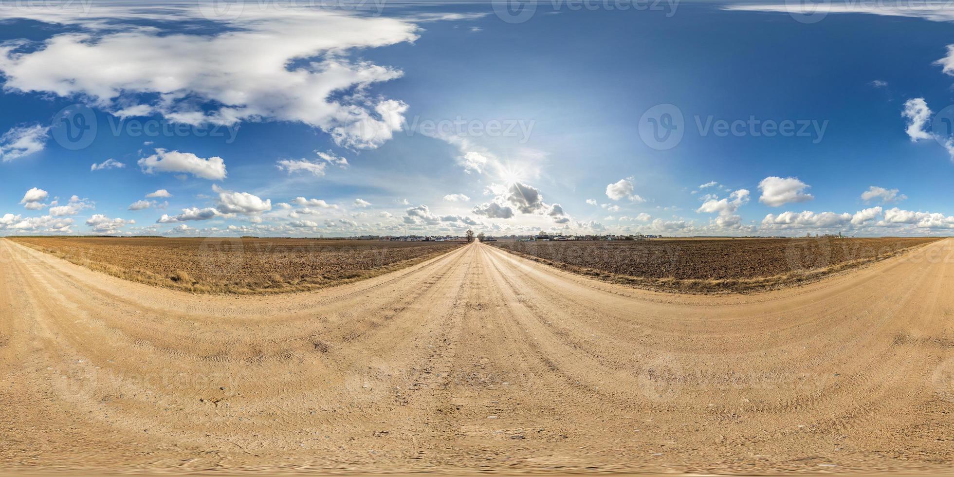 panorama hdri sphérique complet et harmonieux vue à 360 degrés sur la route de gravier parmi les champs au printemps avec des nuages impressionnants en projection équirectangulaire, prêt pour le contenu de réalité virtuelle vr ar photo