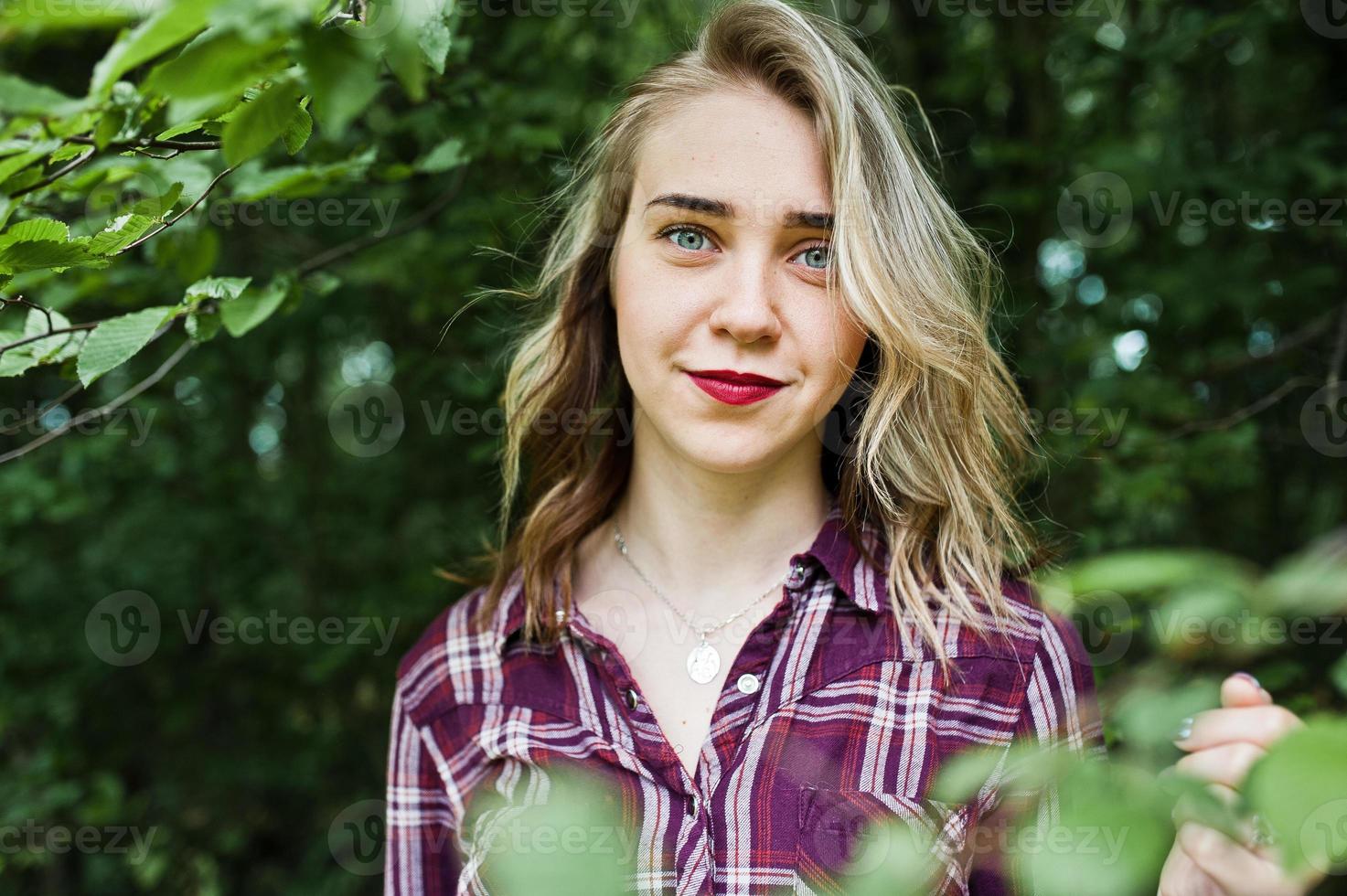 portrait en gros plan d'une jeune fille blonde souriante en chemise tartan à la campagne. photo