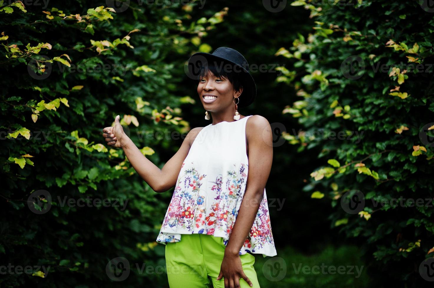 incroyable femme modèle afro-américaine en pantalon vert et chapeau noir posé avec différentes émotions au parc, montre un pouce vers le haut. photo