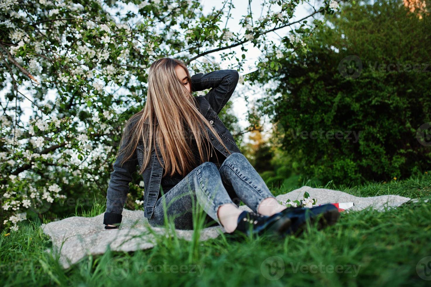 jeune fille brune en jeans assis sur un plaid contre l'arbre de fleurs de printemps. photo