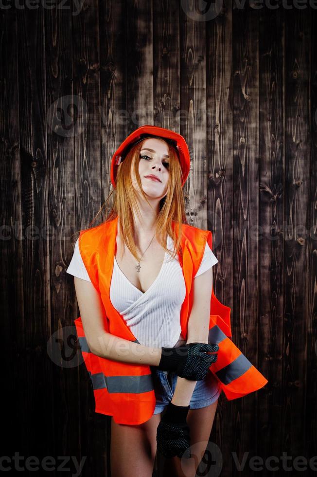 femme ingénieur en orange protège le casque et la veste de construction sur fond de bois. photo