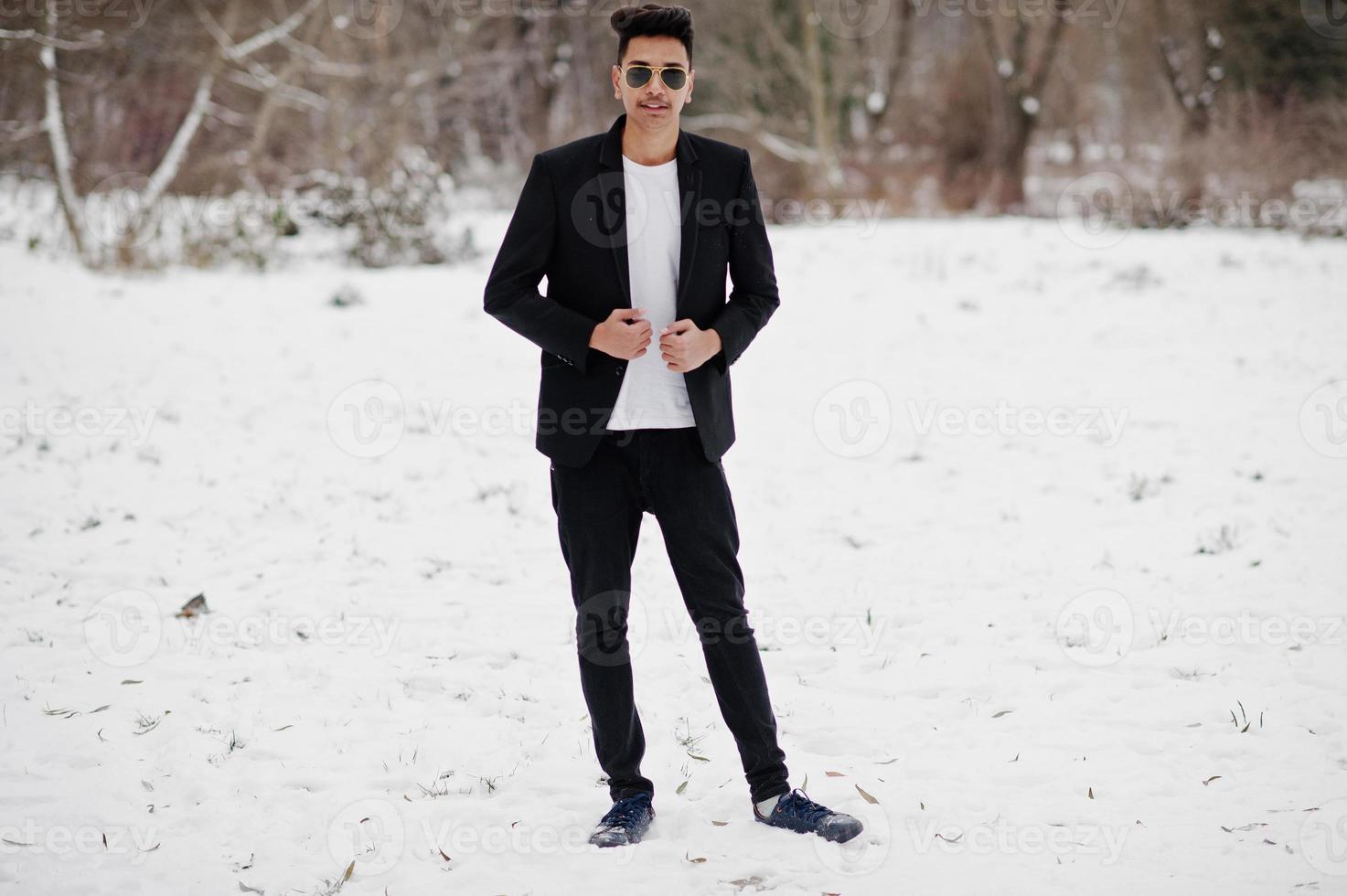 jeune homme indien décontracté en blazer noir et lunettes de soleil posées le jour de l'hiver. photo