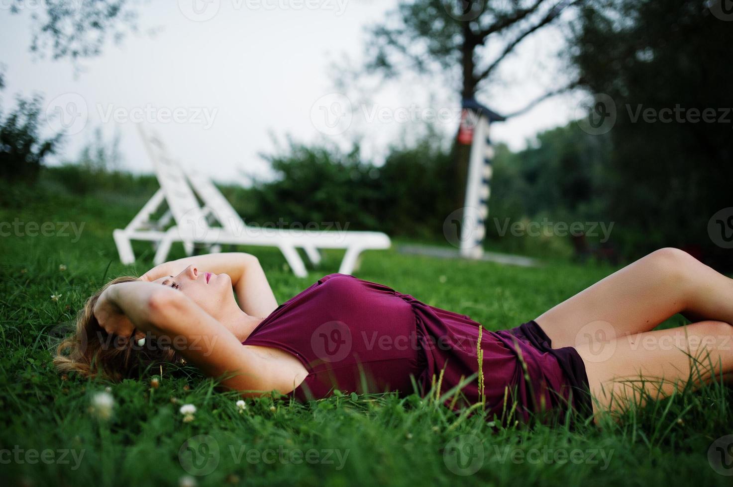 femme sensuelle blonde en robe de marsala rouge allongée dans l'herbe verte. photo
