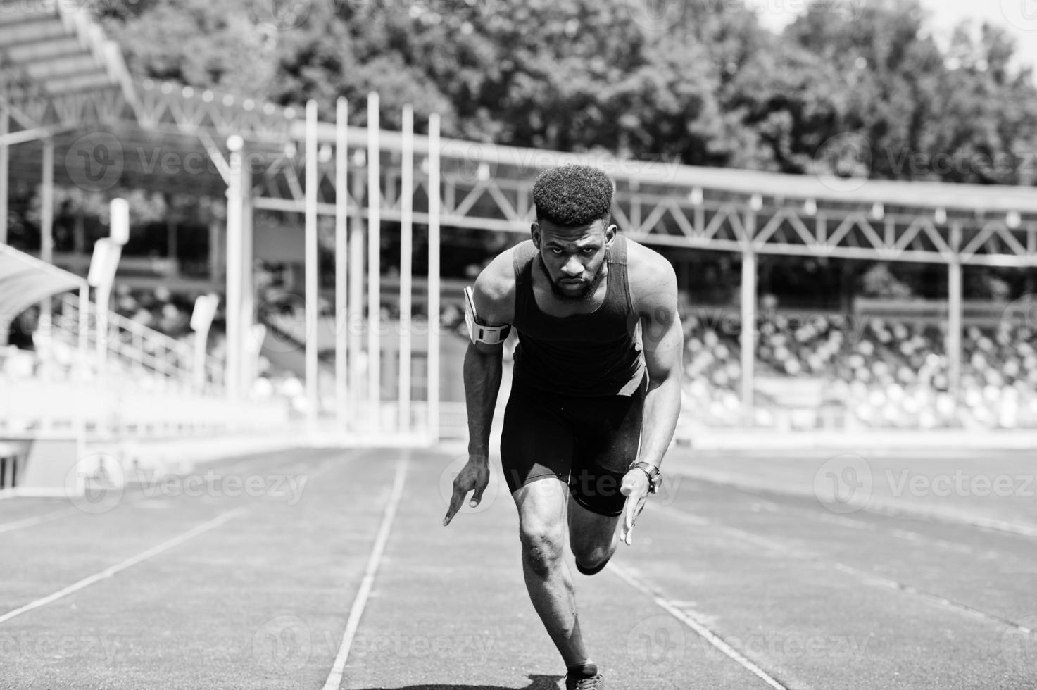 Athlète masculin afro-américain en vêtements de sport faisant la course seul sur une piste de course au stade. photo