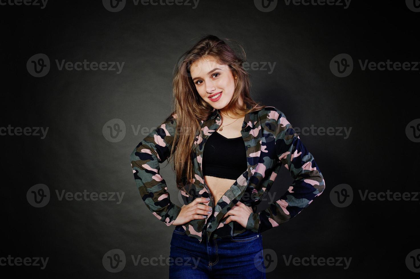 belle fille brune porte une chemise militaire et un jean, posant au studio sur fond gris. portrait de modèle de studio. photo