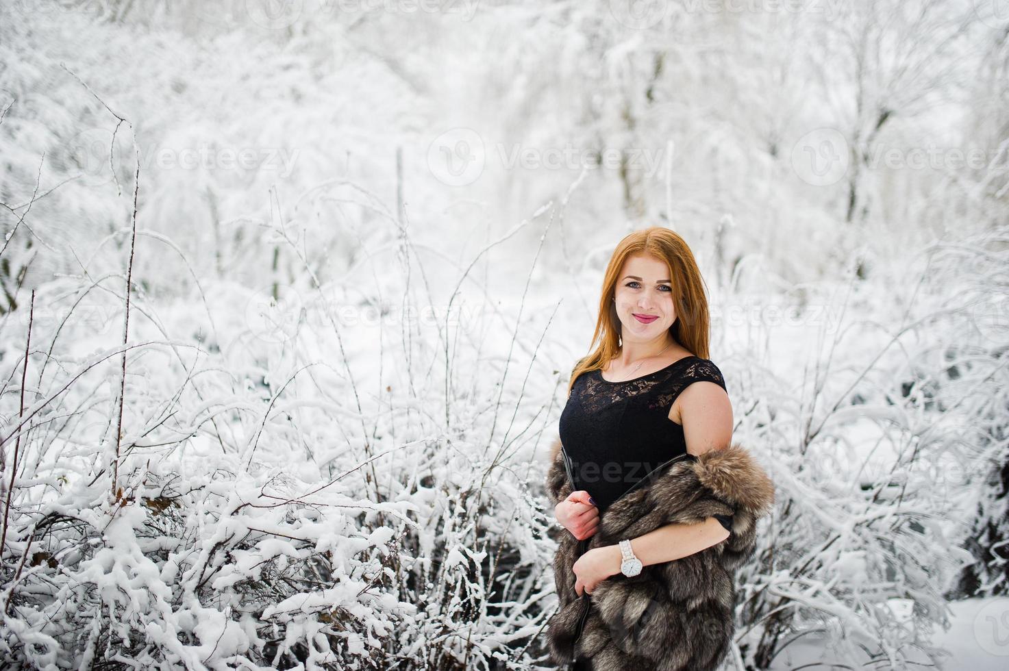 fille aux cheveux rouges en manteau de fourrure marchant au parc enneigé d'hiver. photo