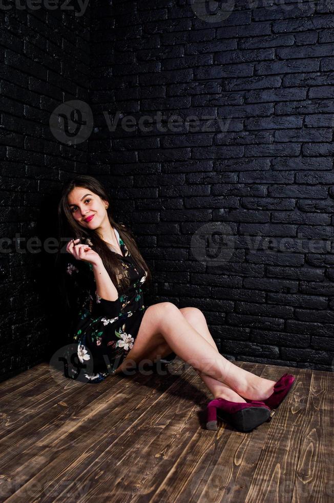 portrait d'une fabuleuse jeune femme en robe à fleurs assise dans le studio sombre. photo