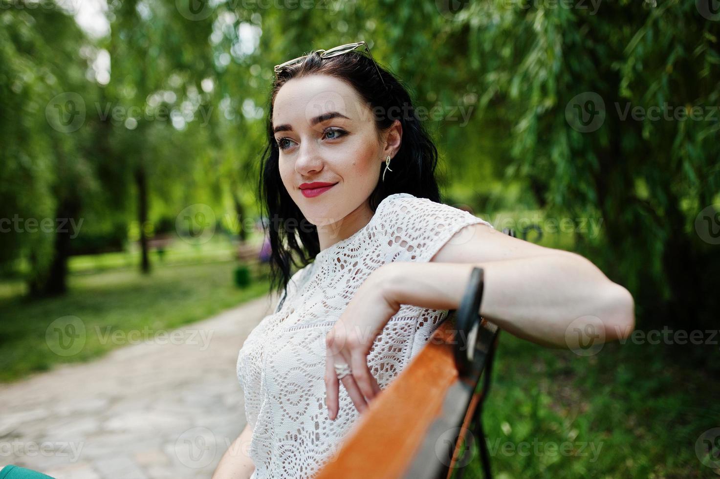 fille brune en jupe verte et chemisier blanc posé au parc, assis sur un banc. photo