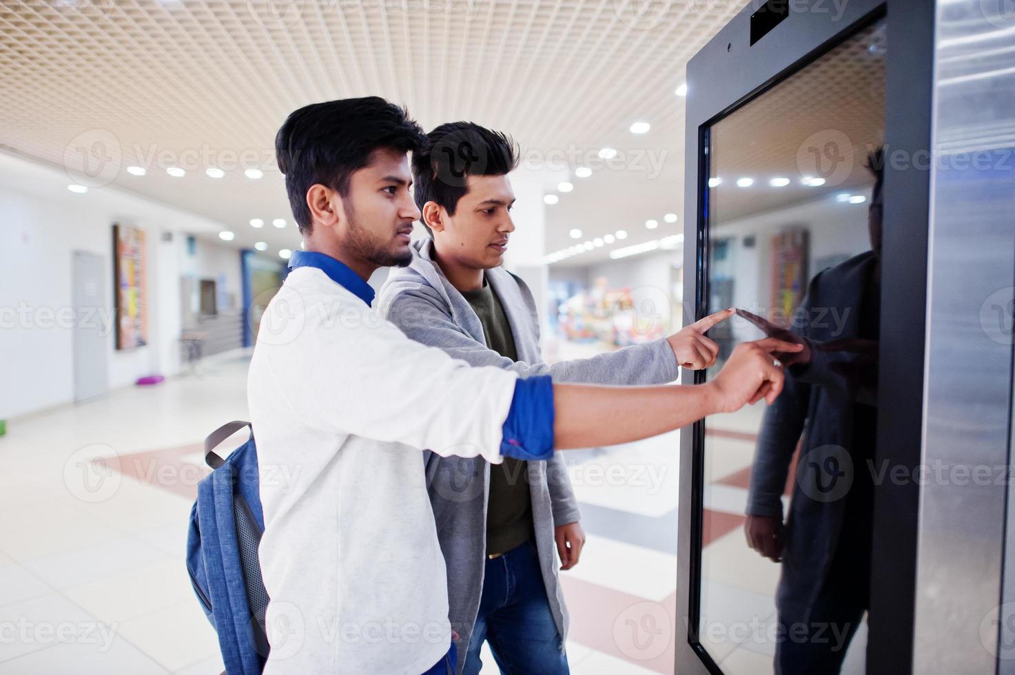 deux gars asiatiques touchant l'écran du bureau d'information électronique dans le centre commercial. photo