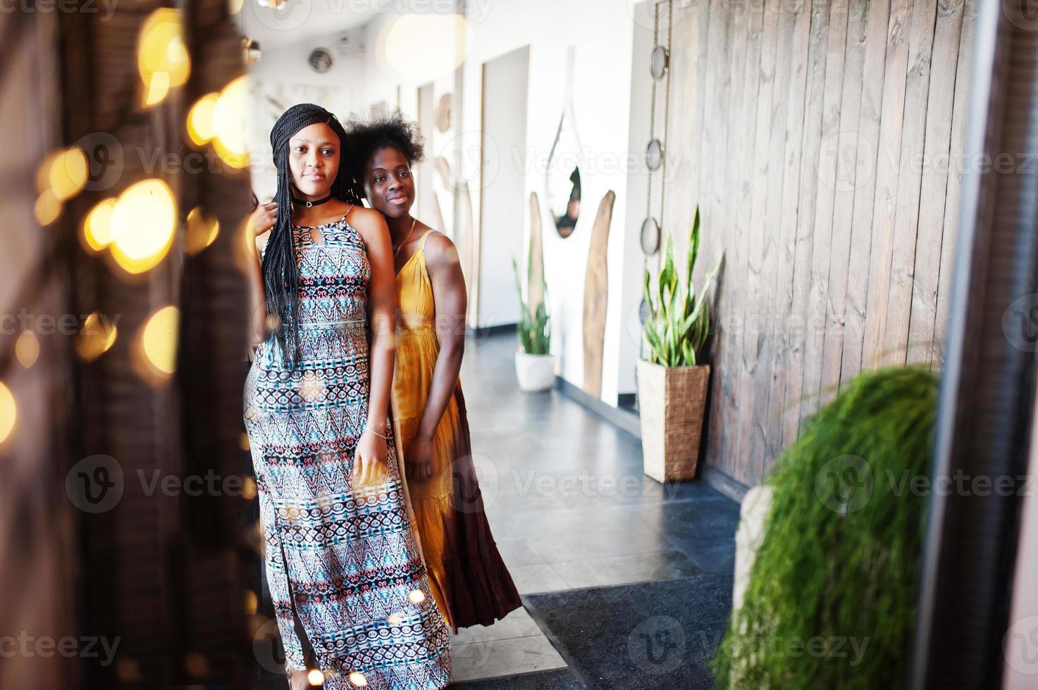 deux copines africaines noires à des robes d'été posées dans un café au miroir. photo