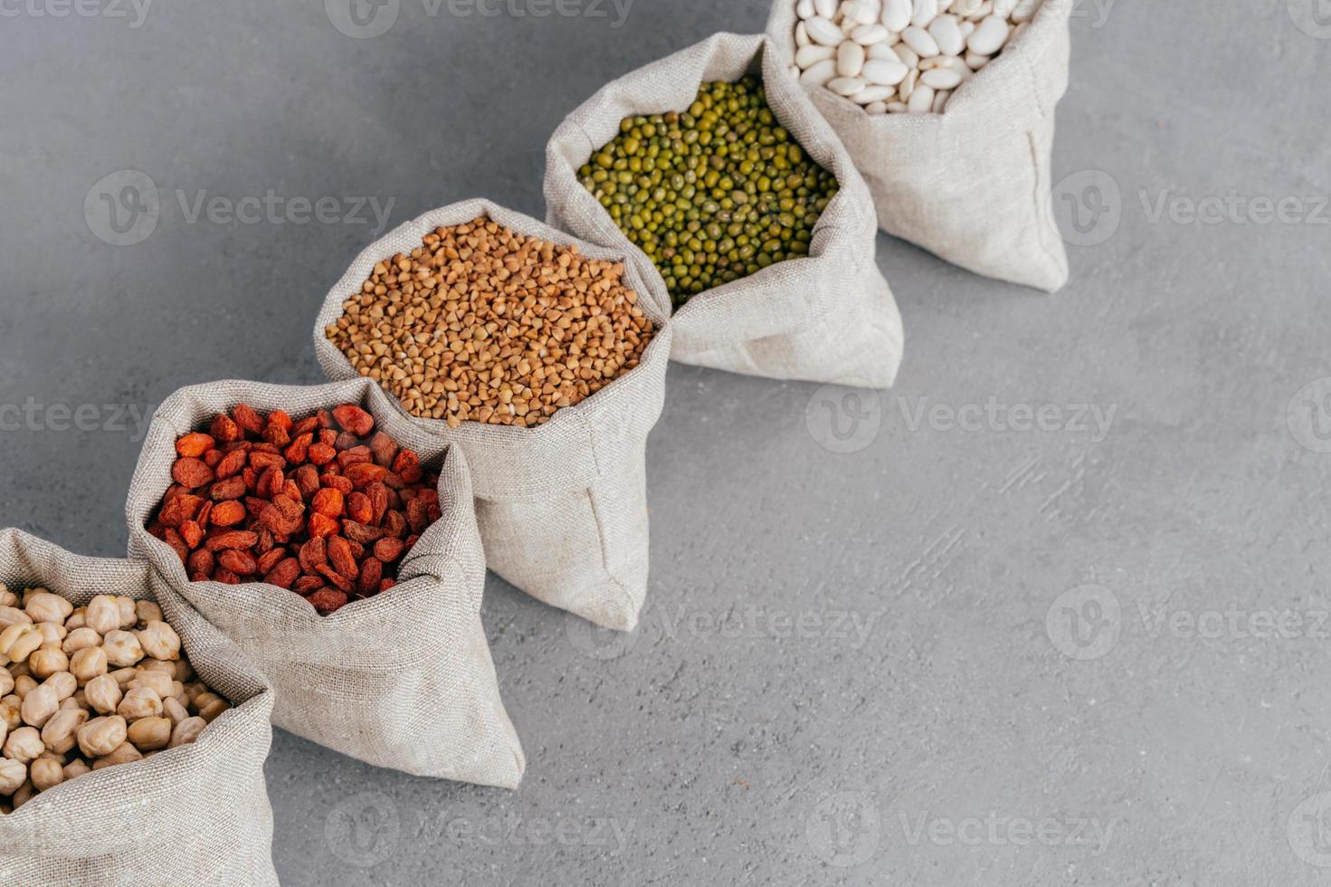 assortiment de grains sans gluten dans des sacs en tissu de lin sur fond gris. sacs remplis de haricots rouges, de lentilles, de sarrasin, de goji et de garbanzo. céréales pour une alimentation saine photo