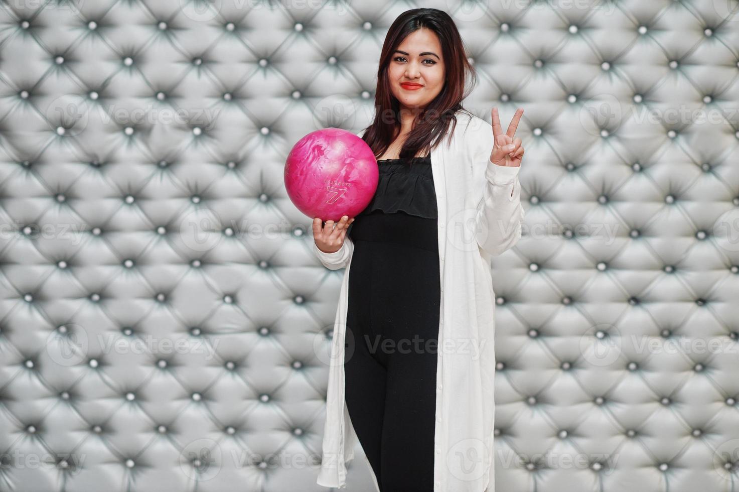 femme asiatique élégante avec boule de bowling rose à portée de main sur fond de mur argenté. photo