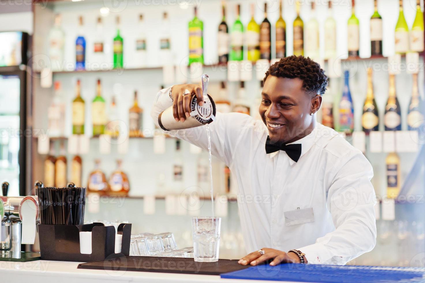 barman afro-américain au bar avec shaker. préparation de boissons alcoolisées. photo