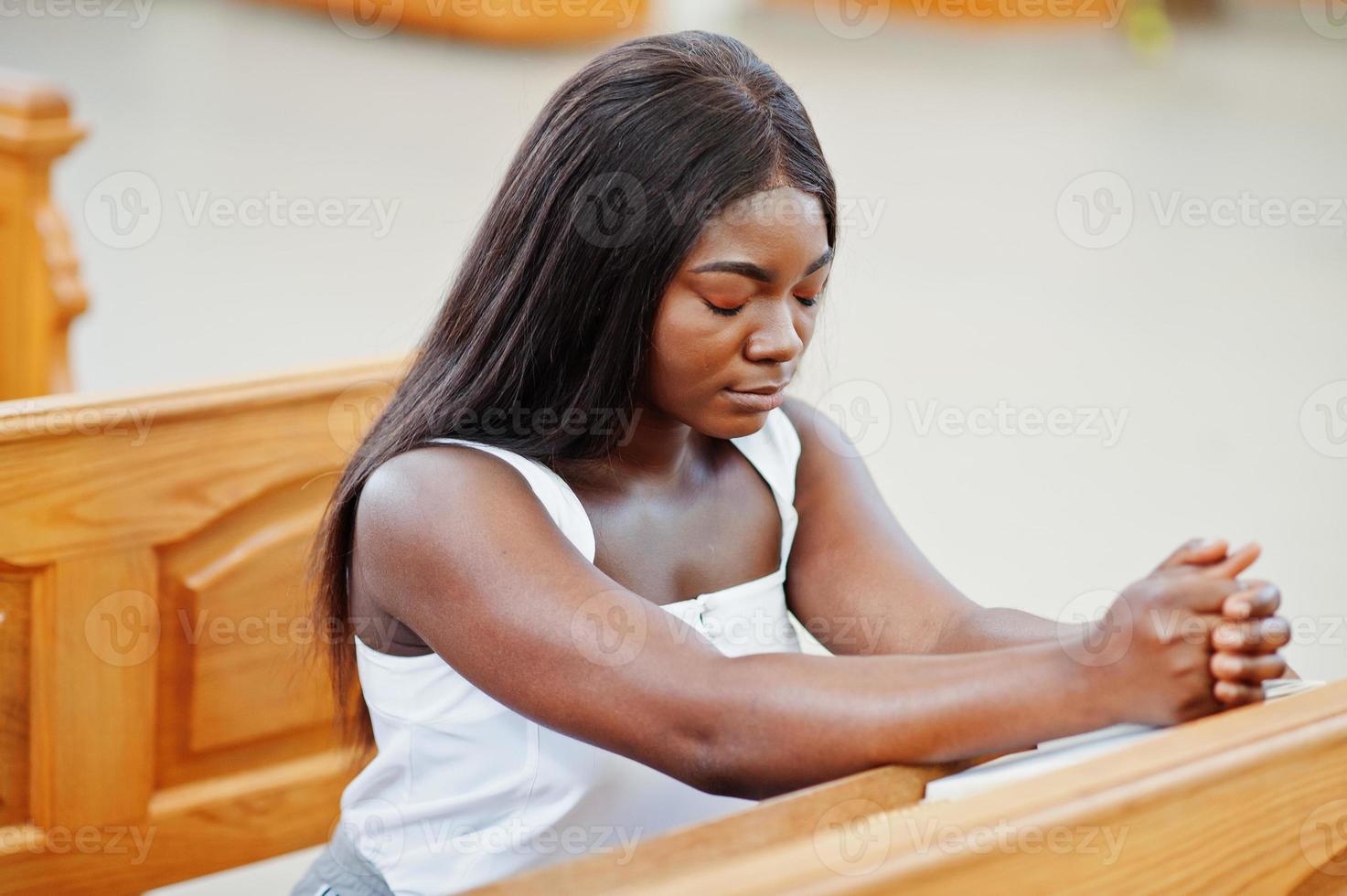 femme afro-américaine priant dans l'église. croyants médite dans la cathédrale et le temps spirituel de la prière. afro girl joint les mains alors qu'il était assis sur un banc. photo