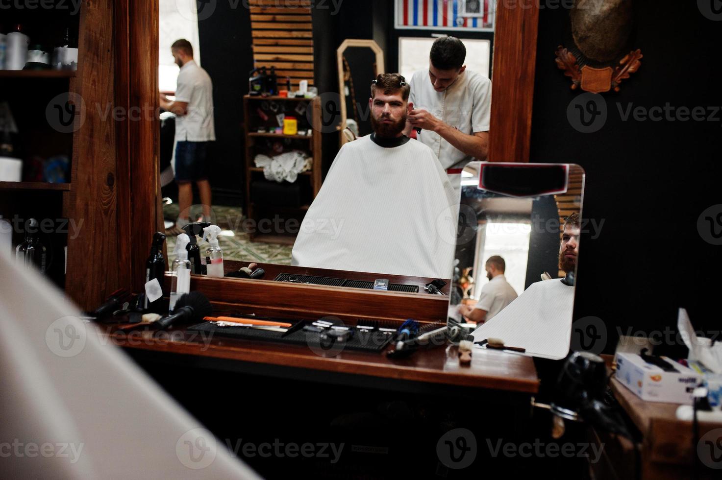 jeune homme barbu se coupe les cheveux par un coiffeur assis sur une chaise au salon de coiffure. âme de barbier. photo