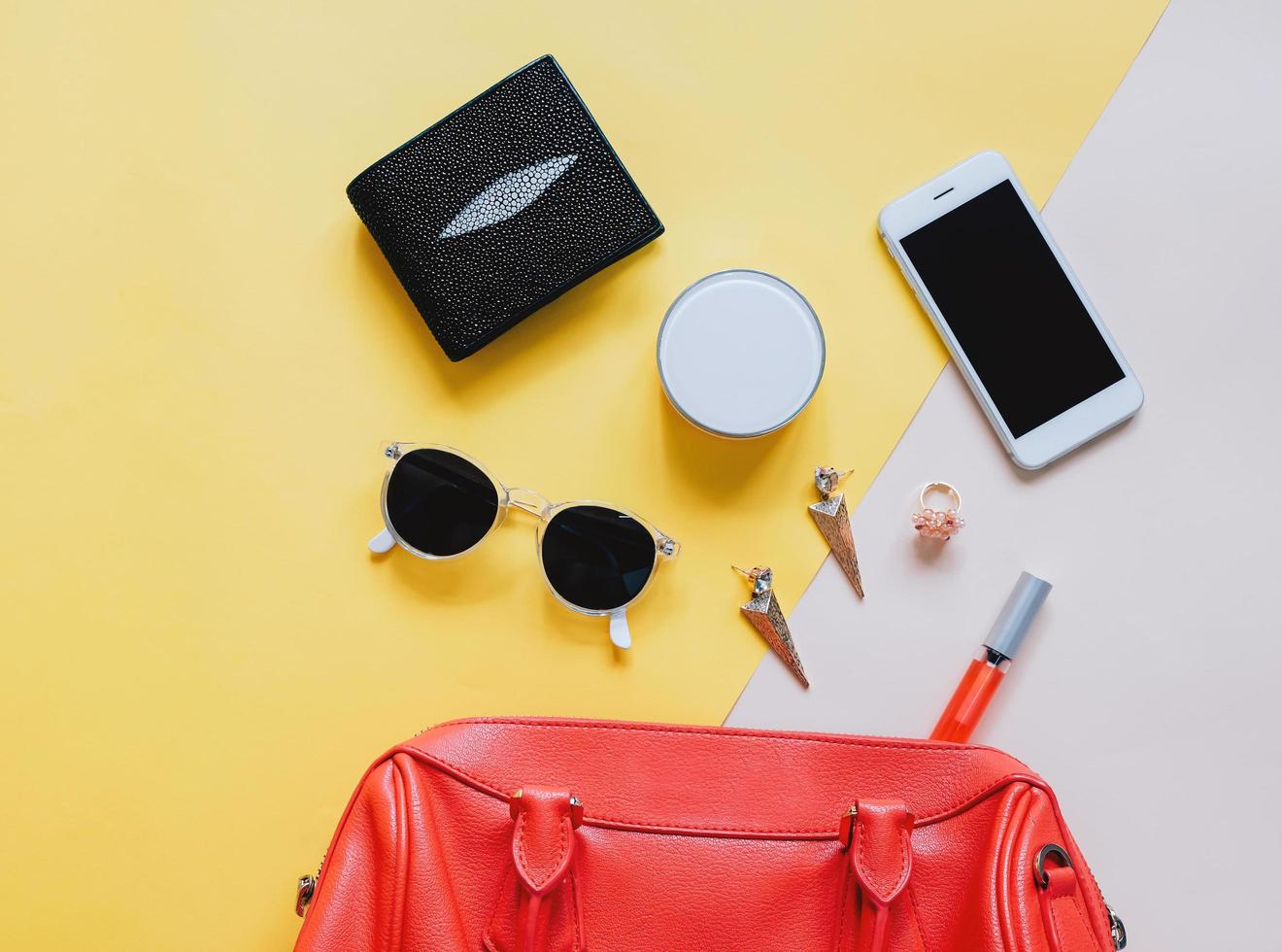 mise à plat d'un sac femme en cuir rouge ouvert avec des cosmétiques, des accessoires, un portefeuille et un smartphone sur fond jaune photo