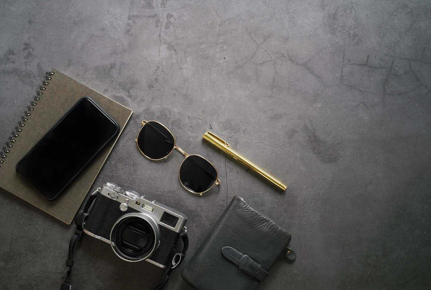 mise à plat du bureau de l'espace de travail des gadgets et accessoires masculins, smartphone, lunettes de soleil, portefeuille, appareil photo et ordinateur portable sur fond de pierre sombre, vue de dessus avec espace de copie, concept d'entreprise et de style de vie