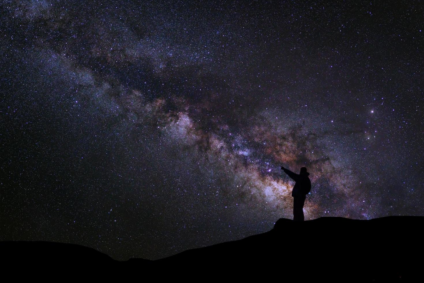 un homme se tient à côté de la galaxie de la voie lactée pointant sur une étoile brillante, une photographie à longue exposition, avec du grain photo