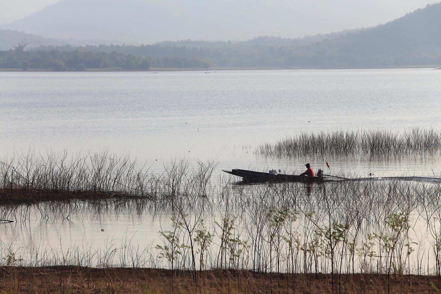 silhouette de pêcheur sur bateau en bois au lac. photo