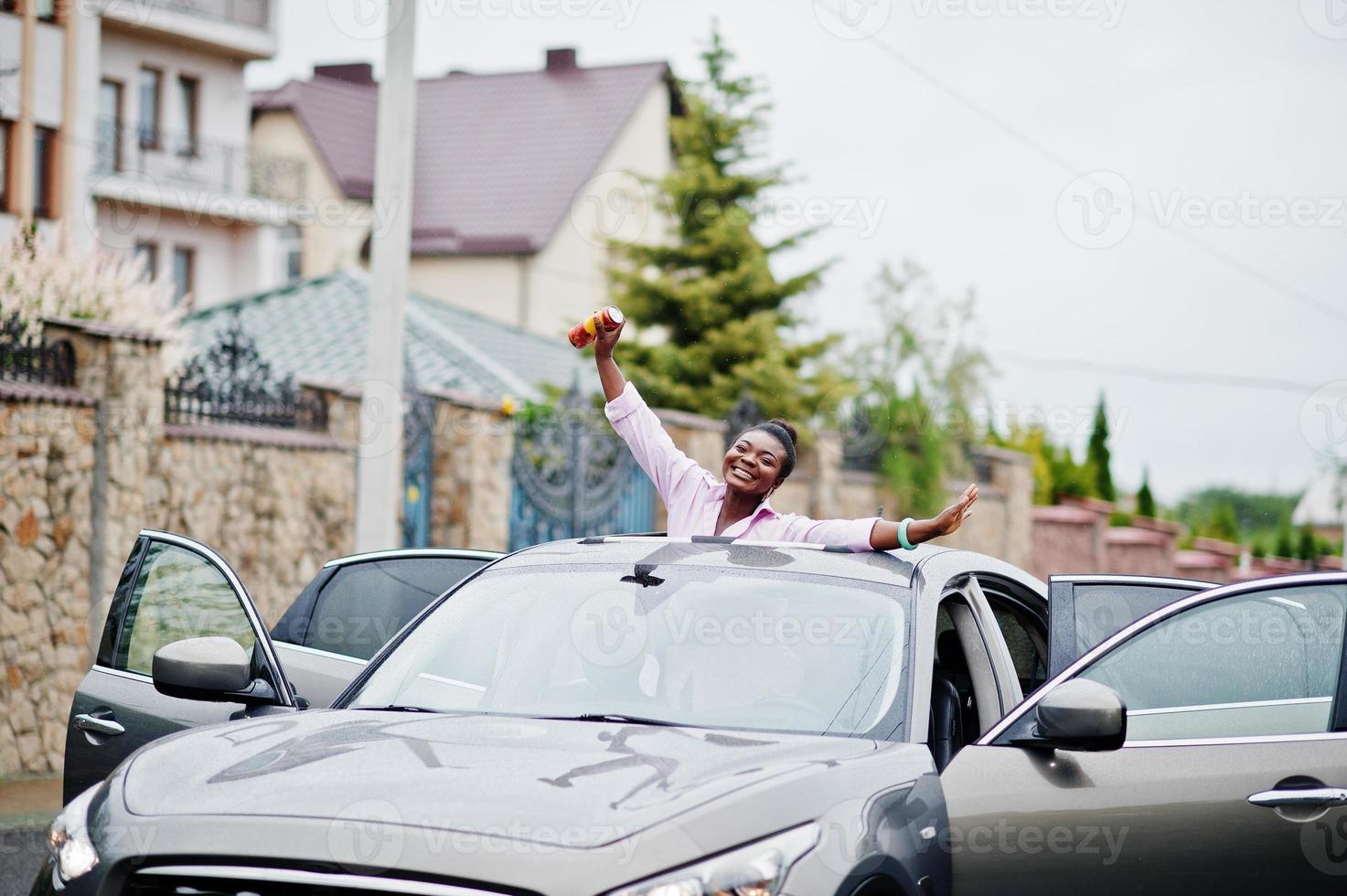 riche femme africaine d'affaires en voiture suv argentée sur le toit ouvrant s'amusant avec de la bière à portée de main. photo