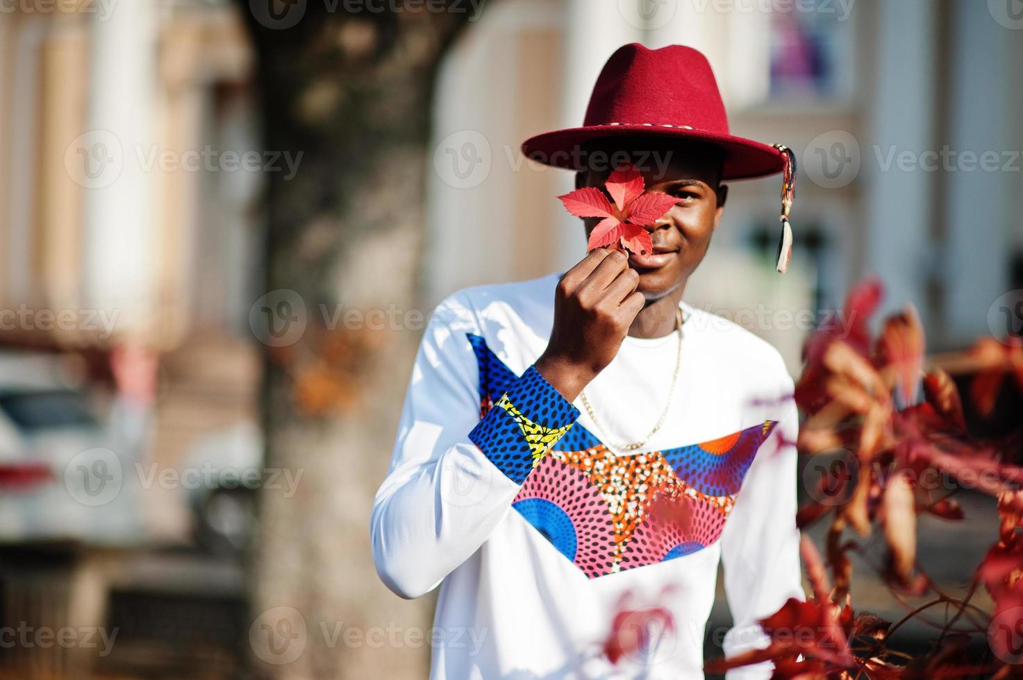 homme afro france élégant et branché en chapeau rouge et tenue blanche posée au jour de l'automne. un modèle africain noir tient des feuilles. photo