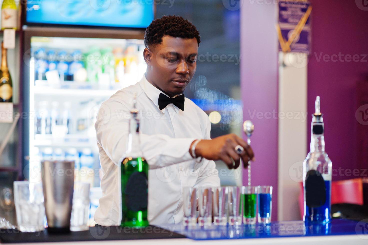 barman afro-américain au bar faisant des cocktails sur des coups. préparation de boissons alcoolisées. photo