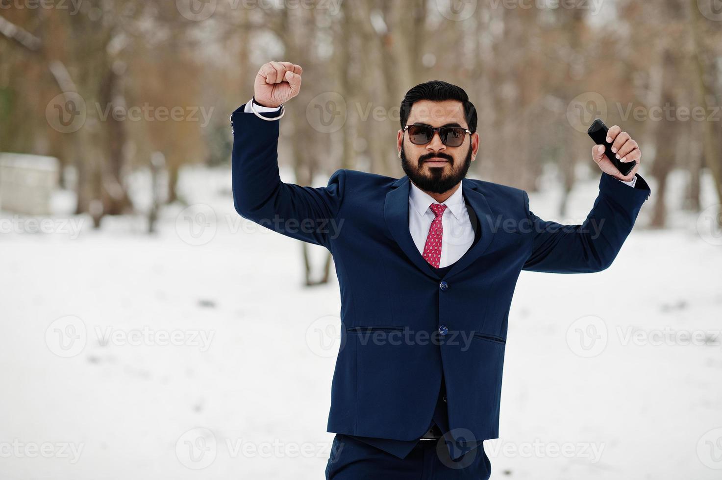 homme d'affaires élégant barbe indienne en costume et lunettes de soleil posées à la journée d'hiver en plein air, mains en l'air et émotions heureuses. photo