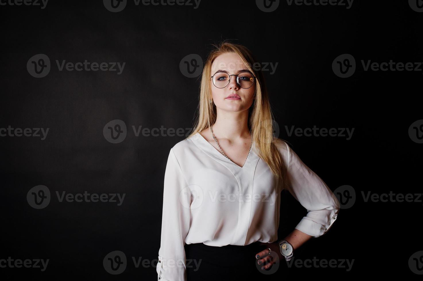 portrait en studio d'une femme d'affaires blonde à lunettes, chemisier blanc et jupe noire sur fond sombre. femme réussie et concept de fille élégante. photo