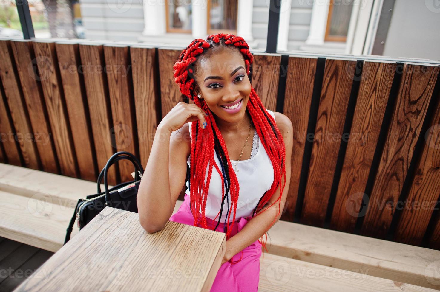 fille afro-américaine à la mode au pantalon rose et aux dreads rouges posées à l'extérieur. photo