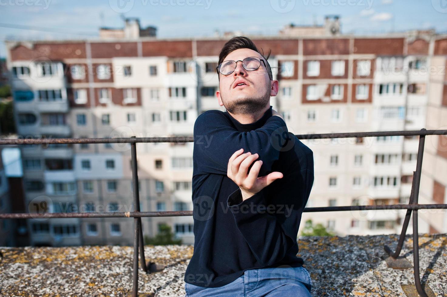 homme macho élégant rêveur en golf noir et lunettes posées sur le toit. photo