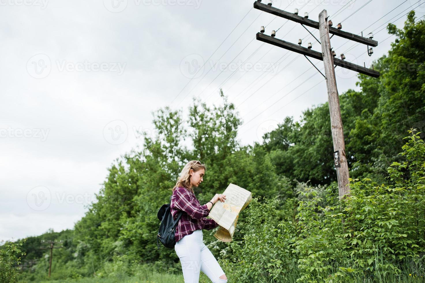 portrait d'une belle fille blonde en chemise tartan marchant avec une carte dans la campagne. photo