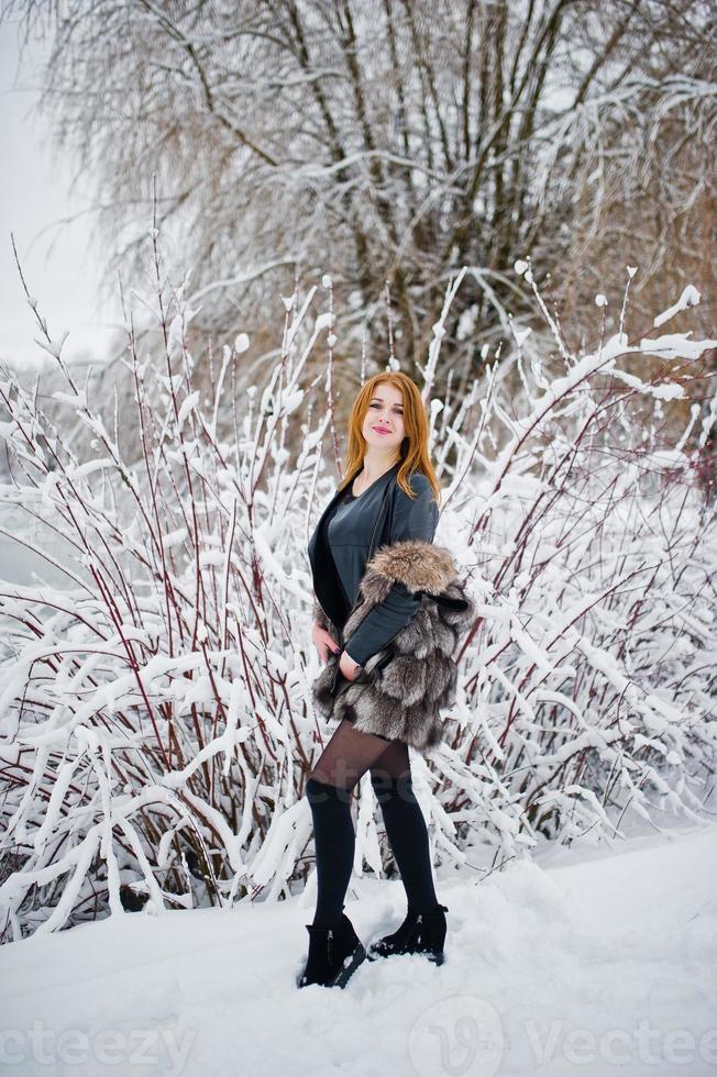 fille aux cheveux rouges en manteau de fourrure marchant au parc enneigé d'hiver. photo