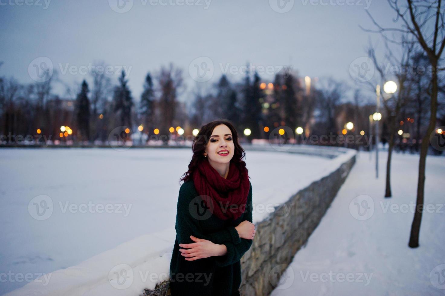 fille brune en pull vert et écharpe rouge en plein air le soir de la journée d'hiver. photo