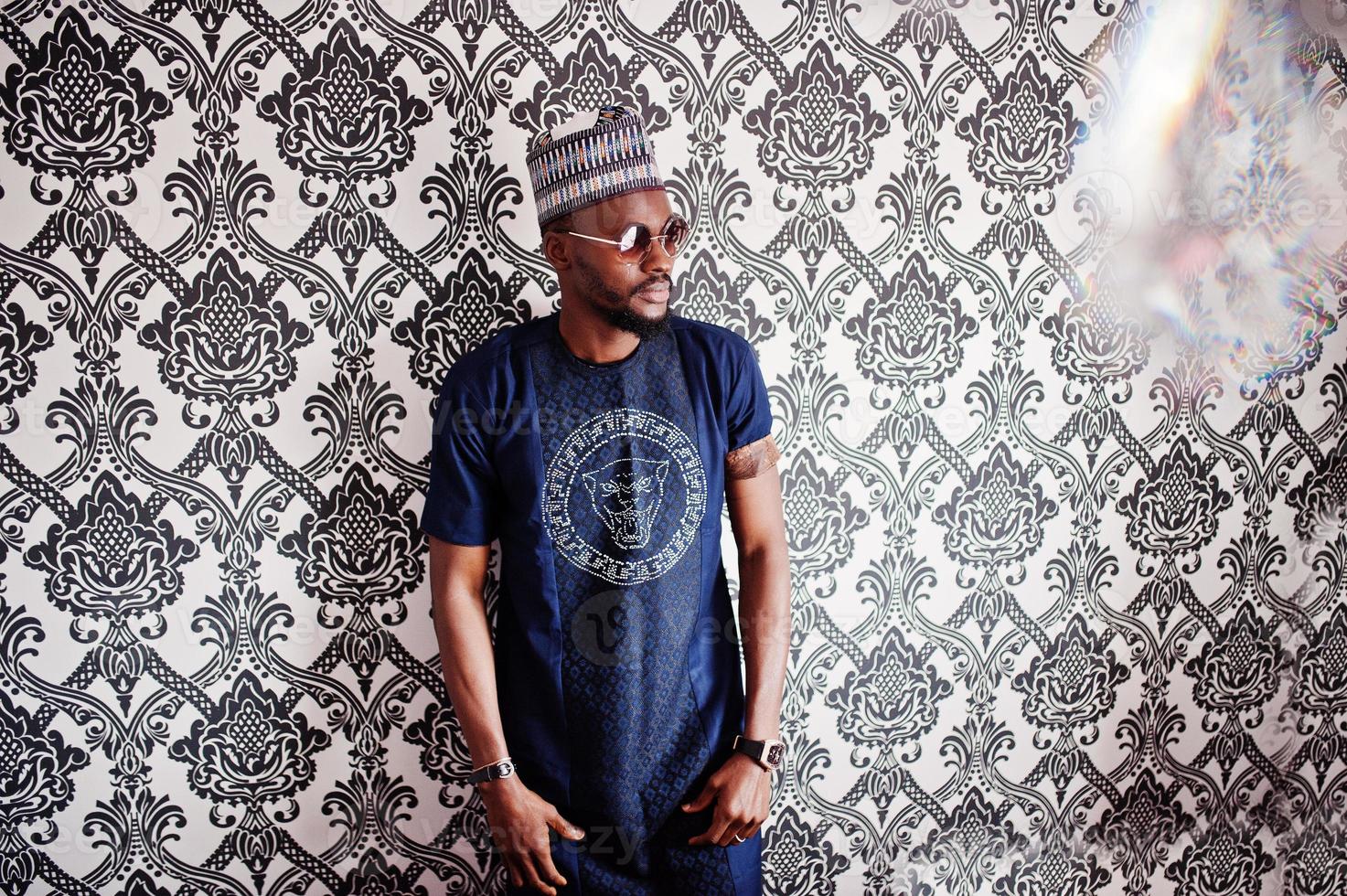 homme africain riche en vêtements traditionnels élégants et chapeau à lunettes posés au studio sur fond vintage. photo