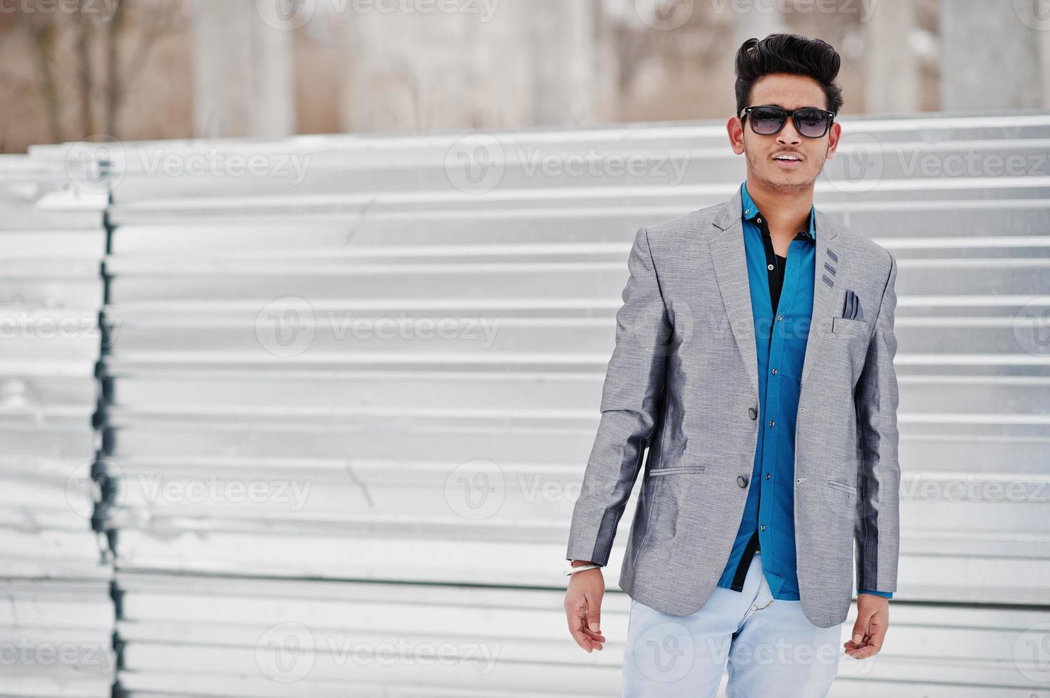 jeune homme indien décontracté en veste argentée et lunettes de soleil posées sur fond d'acier. photo